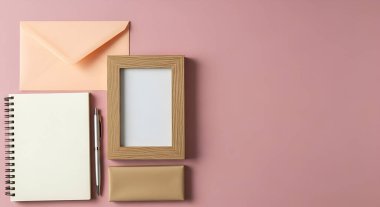 Şeftali rengi bir zarf, ahşap çerçeve, boş bir defter ve yaratıcı projeler için ideal, yumuşak pembe bir yüzeye yerleştirilmiş kalem içeren düz bir kompozisyon..