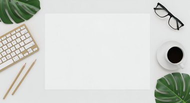 Klavye, kahve fincanı, bardaklar ve tropikal yaprakların yer aldığı temiz, beyaz bir çalışma alanının genel çekimi, sakin ve üretken bir atmosfer yaratıyor..