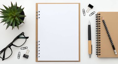 Boş bir not defteri, sulu bir bitki, gözlük ve beyaz bir yüzeye yerleştirilmiş çeşitli kırtasiye malzemelerinin yer aldığı temiz ve düzenli bir çalışma alanı.