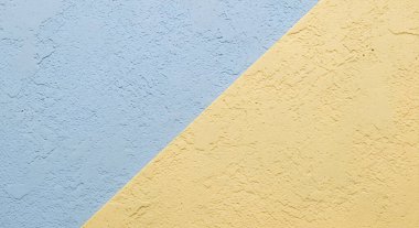 Pastel mavisi ve sarıya boyanmış bir duvar, kaba bir yüzeye sahip soyut bir arkaplan yaratıyor..