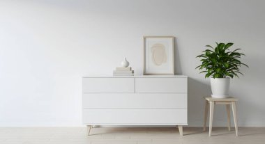 Beyaz bir şifonyer, saksı bitkisi ve çerçevelenmiş sanat eserlerini beyaz bir duvara karşı sergiliyor. Ev dekorasyonu için modern bir iç mekan yaratıyor..