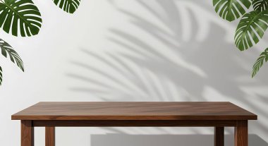 Tahta bir masa, yaprakların gölgeli beyaz bir duvarın önünde durur. Ürün modellemeleri veya yaşam tarzı tasvirleri için mükemmeldir..