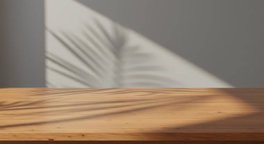 Ahşap bir masa, gri bir duvara yaslanmış, palmiye yaprağı gölgesi ile ürün sergisi için boş bir alan sunuyor..