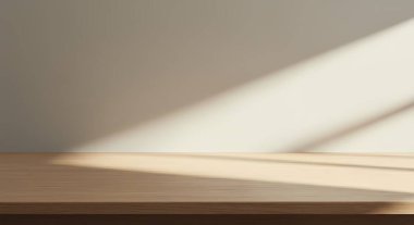 Tahta bir masa, tarafsız bir duvara karşı güneş ışığıyla aydınlatılır ve ürün gösterimi veya sunumu için basit bir zemin oluşturur..