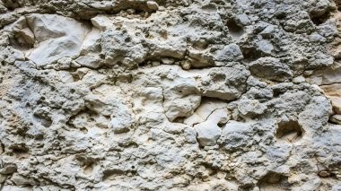 Kaba bir kaya yüzeyine yakın çekim, görünür gözenekleri ve granüler dokusuyla açık ve koyu gölgelerin karışımını içerir..
