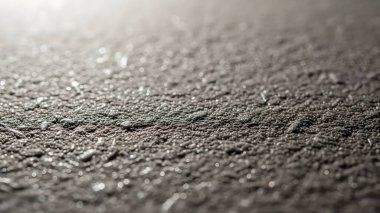 Kaba bir asfalt yol yüzeyinin detaylı görüntüsü, materyalin dokusunu ve bileşimini vurguluyor. Kaba, tanecikli detaylara odaklan..
