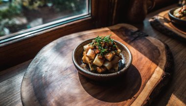 Küçük bir kase kızarmış patates küpü ve doğranmış otlar pencerenin kenarındaki yuvarlak tahta bir tahtada sıcak, doğal ışıkla yıkanır..
