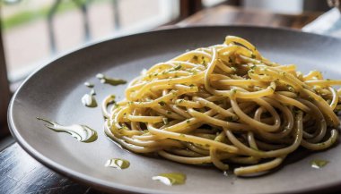 Sarımsak yağlı, pürüzsüz makarna ve yumuşak yansımalı doğal ışıkla aydınlatılan karanlık bir tabakta otlar.