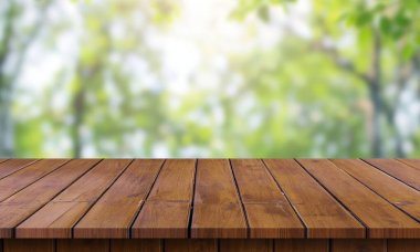 Ahşap bir masa açık havada, bulanık yeşil bir yeşillik arka planda oturuyor..