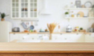 Parlak, bulanık mutfak sahnesi, odağında ahşap bir tezgah, temiz beyaz bir zemin, yumuşak doğal ışık, sakin bir ev atmosferi yaratıyor..