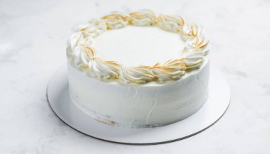 Zarif bir kutlama için arka planda çekilen altın sarısı bir çelenkle süslenmiş el değmemiş beyaz bir pasta.