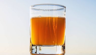 Işıl ışıl portakal suyuyla dolu uzun bir bardak parlak bir arkaplanda duruyor, taze narenciye rengi ve parlak yansıması olan berrak bir sıvı sergiliyor..