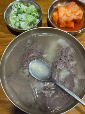 A hearty bowl of gukbap, a traditional Korean dish combining rich, flavorful broth with rice, often accompanied by tender meat and seasoned with green onions, garlic, and spicy sauces for a comforting meal.