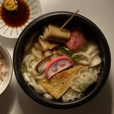 A bowl of udon noodles in a savory broth, topped with green onions, tempura, and a soft boiled egg. The thick, chewy noodles and rich flavors make it a comforting Japanese classic.