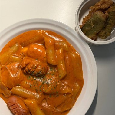 Çiğnenmiş kırmızı soslu pirinç kekleri ve susam tohumları ve yeşil soğanla kaplı baharatlı Kore tteokbokki. Bağımlılık yaratan tadı ve tatmin edici dokusuyla bilinen popüler bir sokak yemeği..