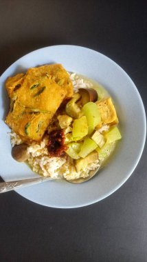 Traditional Indonesian mixed rice meal served on a plate with steamed white rice, assorted side dishes, vegetables, fried tempeh, and sambal, showcasing vibrant colors and rich in close-up detail