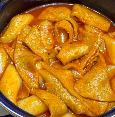 Çiğnenmiş kırmızı soslu pirinç kekleri ve susam tohumları ve yeşil soğanla kaplı baharatlı Kore tteokbokki. Bağımlılık yaratan tadı ve tatmin edici dokusuyla bilinen popüler bir sokak yemeği..