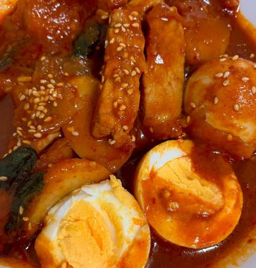 Çiğnenmiş kırmızı soslu pirinç kekleri ve susam tohumları ve yeşil soğanla kaplı baharatlı Kore tteokbokki. Bağımlılık yaratan tadı ve tatmin edici dokusuyla bilinen popüler bir sokak yemeği..