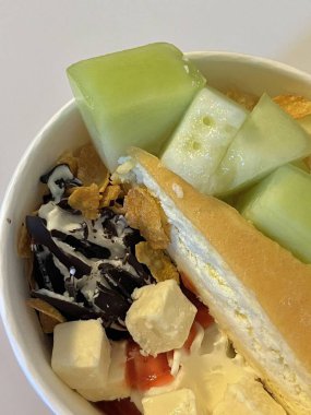 Doldurulmuş yoğurtlu tatlı bir fincanda servis ediliyor, pürüzsüz kremalı dokular, parlak yüzeyli, taze meyve parçaları ile kaplı, ferahlatıcı ve davetkar görünümünü detaylıca vurgulayan.