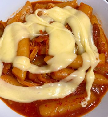 Çiğnenmiş kırmızı soslu pirinç kekleri ve susam tohumları ve yeşil soğanla kaplı baharatlı Kore tteokbokki. Bağımlılık yaratan tadı ve tatmin edici dokusuyla bilinen popüler bir sokak yemeği..