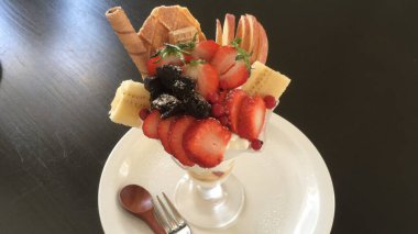 Taze meyveyle yapılmış çilekli parfe ve kırsal beyaz bir masanın üzerinde yoğurt. Bulanık arkaplan ve arkaplan ile seçmeli odak.