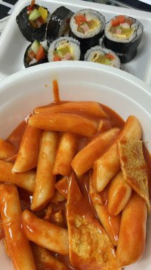 Çiğnenmiş kırmızı soslu pirinç kekleri ve susam tohumları ve yeşil soğanla kaplı baharatlı Kore tteokbokki. Bağımlılık yaratan tadı ve tatmin edici dokusuyla bilinen popüler bir sokak yemeği..