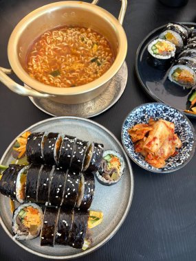 Kimbap ve Ramyun, mükemmel bir Kore karışımı! Lezzetli pirinç rulolarının yanında sebze, et ve turşu ile baharatlı ve rahatlatıcı ramen ye. Günün her saatinde doyurucu bir yemek..
