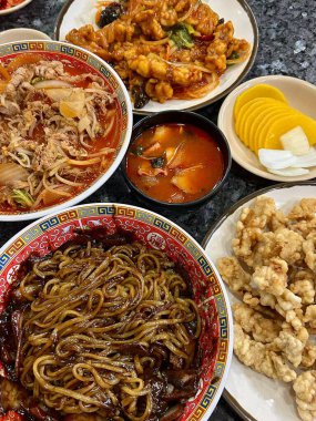 Jjampong and Jajangmyeon are two iconic Korean-Chinese noodle dishes. Jjampong is a spicy seafood noodle soup with vegetables, while Jajangmyeon features noodles topped with a savory black bean sauce.