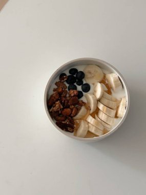 Taze renkli meyvelerle kaplı bir kasede servis edilen Yunan yoğurdu, kremalı pürüzsüz bir doku, canlı doğal renkler ve detaylı bir şekilde ferahlatıcı bir görünüş sunuyor.