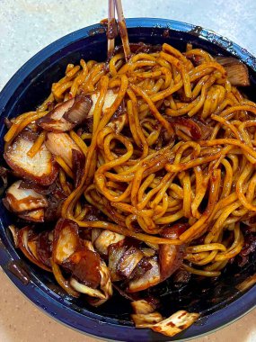 Bol siyah fasulye soslu kalın erişteli klasik jajangmyeon. Dilimlenmiş salatalık ve susam tohumlarıyla süslenmiş. Çok sevilen bir Kore-Çin konfor yemeği, lezzet ve derinlik dolu..