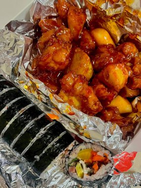 Güzel dilimlenmiş kimbap rulolarının yanında servis edilen kızarmış Kore tavuğu leziz ve görsel olarak çekici bir kombinasyon yaratıyor.