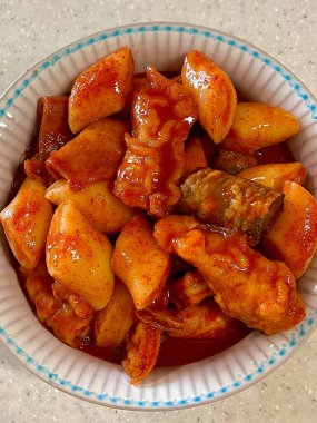 Çiğnenmiş kırmızı soslu pirinç kekleri ve susam tohumları ve yeşil soğanla kaplı baharatlı Kore tteokbokki. Bağımlılık yaratan tadı ve tatmin edici dokusuyla bilinen popüler bir sokak yemeği..