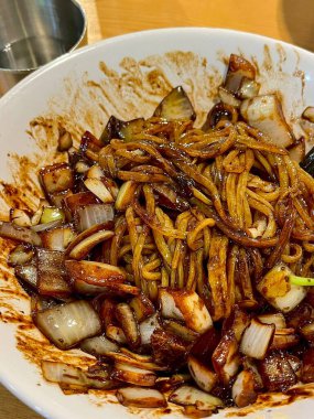 Bol siyah fasulye soslu kalın erişteli klasik jajangmyeon. Dilimlenmiş salatalık ve susam tohumlarıyla süslenmiş. Çok sevilen bir Kore-Çin konfor yemeği, lezzet ve derinlik dolu..