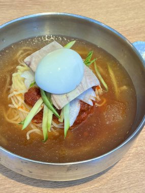Naengmyeon, üzerine dilimlenmiş sebze, haşlanmış yumurta ve baharatlı sos serpilmiş soğuk Kore erişte tabağı. Yaz yemeği fotoğrafçılığı ve Kore mutfağı projeleri için mükemmel..