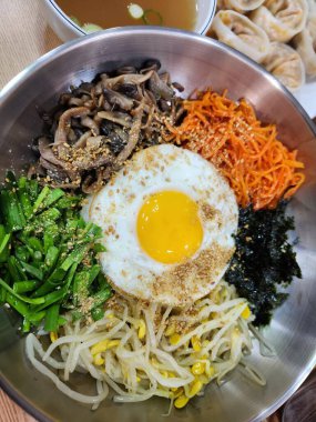 Bibimbap, çeşitli sebzeler, gochujang ve sıklıkla dilimlenmiş etin eşlik ettiği kızarmış yumurta ile süslenmiş canlı bir Kore pirinç yemeği. Karıştırıldığında, aromalı ve dengeli olur..