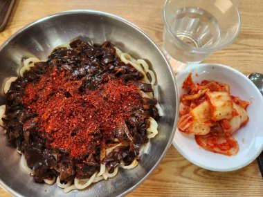 Bol siyah fasulye soslu kalın erişteli klasik jajangmyeon. Dilimlenmiş salatalık ve susam tohumlarıyla süslenmiş. Çok sevilen bir Kore-Çin konfor yemeği, lezzet ve derinlik dolu..