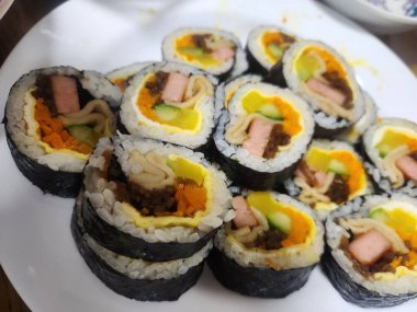 Taze sebzelerle, baharatlı pirinçlerle ve gevrek yosunlara sarılmış lezzetli proteinlerle dolu nefis kimbap dürümleri. Her ısırıkta lezzet ve dokuların mükemmel bir kombinasyonu.