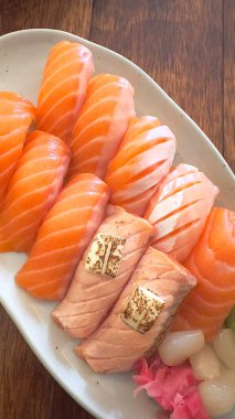 Mükemmel şekilli pirincin üzerine parlak turuncu dilimli taze somon balığı. Basit, renkli ve iştah açıcı bir sunum için yeşil yapraklar ve turpla süslenmiş.