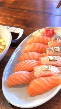 Mükemmel şekilli pirincin üzerine parlak turuncu dilimli taze somon balığı. Basit, renkli ve iştah açıcı bir sunum için yeşil yapraklar ve turpla süslenmiş.