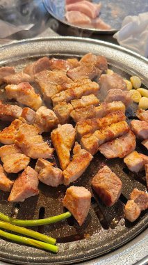Izgara samgyeopsal, kalın domuz eti dilimleri çıtır çıtır ve taze et. Klasik bir Kore barbekü deneyimi için marul, sarımsak ve sosla servis ediliyor..