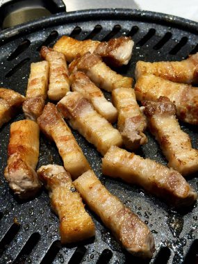 Izgara samgyeopsal, ızgarada pişen domuz eti dilimleri. Lezzetli bir yemek deneyiminin özünü yakalayan popüler bir Kore barbekü yemeği..