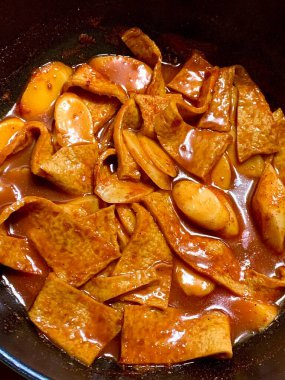 Çiğnenmiş kırmızı soslu pirinç kekleri ve susam tohumları ve yeşil soğanla kaplı baharatlı Kore tteokbokki. Bağımlılık yaratan tadı ve tatmin edici dokusuyla bilinen popüler bir sokak yemeği..