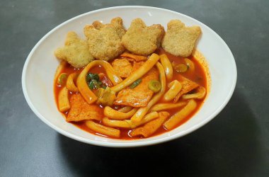 Çiğnenmiş kırmızı soslu pirinç kekleri ve susam tohumları ve yeşil soğanla kaplı baharatlı Kore tteokbokki. Bağımlılık yaratan tadı ve tatmin edici dokusuyla bilinen popüler bir sokak yemeği..