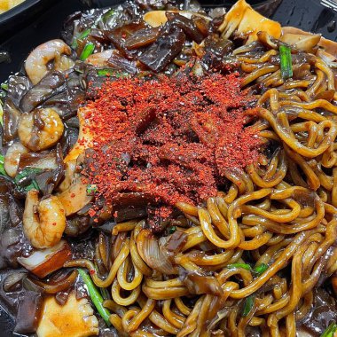 Bol siyah fasulye soslu kalın erişteli klasik jajangmyeon. Dilimlenmiş salatalık ve susam tohumlarıyla süslenmiş. Çok sevilen bir Kore-Çin konfor yemeği, lezzet ve derinlik dolu..