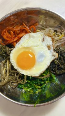 Bibimbap, çeşitli sebzeler, gochujang ve sıklıkla dilimlenmiş etin eşlik ettiği kızarmış yumurta ile süslenmiş canlı bir Kore pirinç yemeği. Karıştırıldığında, aromalı ve dengeli olur..