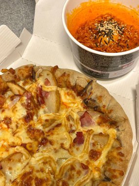 Canlı kırmızı soslu baharatlı buldakmyeon eriştesi peynirli pizzanın yanında servis edilir. Sıcak ve tuzlu, doyurucu bir öğünde zengin lezzetlerin cesur bir kombinasyonunu yaratır.