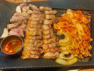 Izgara samgyeopsal, kalın domuz eti dilimleri çıtır çıtır ve taze et. Klasik bir Kore barbekü deneyimi için marul, sarımsak ve sosla servis ediliyor..