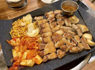 Izgara samgyeopsal, kalın domuz eti dilimleri çıtır çıtır ve taze et. Klasik bir Kore barbekü deneyimi için marul, sarımsak ve sosla servis ediliyor..