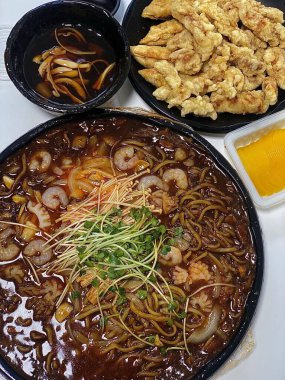 Zengin siyah fasulye sosuna bulanmış kalın, çiğnenmiş erişteli klasik Kore-Çin karışımı, yanında gevrek tangsuyuk, bol yağda kızartılmış domuz eti ve tatlı ve ekşi sos servis edilir..