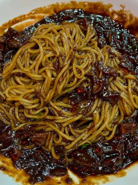 Bol siyah fasulye soslu kalın erişteli klasik jajangmyeon. Dilimlenmiş salatalık ve susam tohumlarıyla süslenmiş. Çok sevilen bir Kore-Çin konfor yemeği, lezzet ve derinlik dolu..